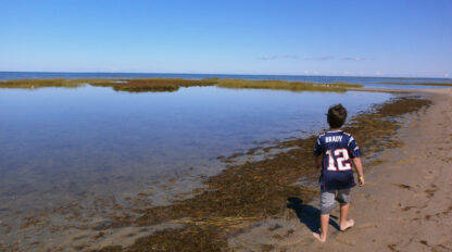 young child walking along the beach with a Tom Brady football shirt on